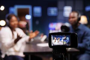 Professional camera on a tripod records african american couple doing a talk show from home for an online audience. Digital device films a conversation between interviewer and celebrity. photo