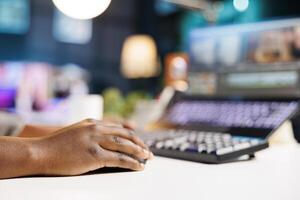 Close-up of African American hand holding digital mouse browsing on her laptop. Detailed view of a black person using a pointer while editing and creating content on a personal computer. photo