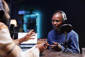 Black man radio show host holds live chat with guest and records the interaction for audience to hear live. Influencer speaking with journalist and broadcasting the debate to online fans at home. photo