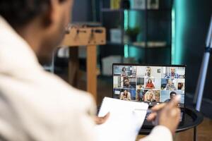 Remote employee in conference meeting chatting with multi ethnic international team while working from home. Self employed man in online call with coworkers in apartment photo