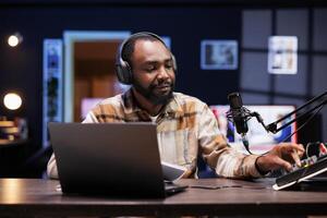 African american content creator adjusting knobs on sound mixer for good audio quality while recording a vlog. Black male blogger using professional equipment for filming channel intro for viewers. photo