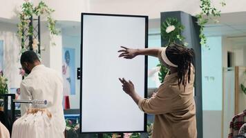 BIPOC client in clothing store using augmented reality mockup screen to look at clothes options to try on. Customer using led kiosk to visualize outfits in showroom before buying photo