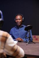 Black male guest speaking into microphone, answering questions from radio program host. African american man being interviewed using audio equipment to record an online talk show at home. photo