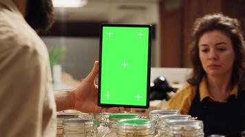 Customer uses mockup tablet in zero waste supermarket to check ingredients for healthy recipe, close up. Client in eco bio local shop with green screen device while shopping for pantry staples photo