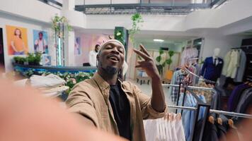 Man filming POV vlog while doing shopping in elegant fashion boutique, giving viewers info. Influencer doing social media content in clothing store, promoting clothing store new collection stock photo