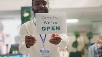 Smiling storekeeper finally reopening store after restocking elegant high end fashion boutique. Man turning closed sign from clothing store door after adding new collection, close up photo