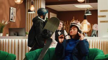 Man asking staff about winter sports while he carries snowboard in mountain resort lobby, hospitality industry during wintertime. Hotel guest eager to have fun on slope with leisure activity. Handheld shot. photo