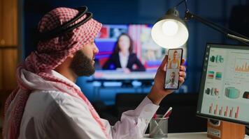 Muslim teleworker and coworkers in online call checking analytics statistical data sets in dimly lit apartment. Arab employee optimizing key performance indicators in teleconference meeting photo