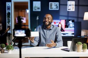 Smiling content creator at home with product waiting to be unboxed in front of him while he does introduction. Trending influencer doing unboxing footage for viewers photo