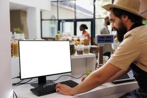 Caucasian vendor at counter using white screen on computer, showing isolated chromakey display on pc monitor. Male small business owner encouraging healthy lifestyle with blank mockup template. photo