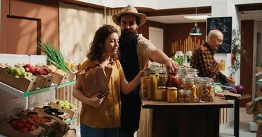 Client using paper bag in pesticides free food shop, inquiring about products ethical sourcing. Woman in local store with no singe use plastics policy chatting with trader about pantry staples photo