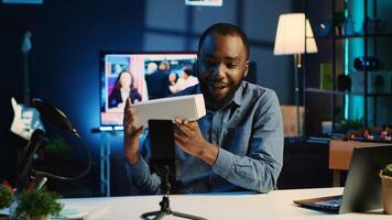 Tech content creator filming packaged product unboxing in neon lights personal home studio using professional equipment. Influencer showing sponsoring partner merchandise, urging subscribers to buy it photo