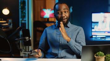 African american content creator using selfie stick smartphone, doing live broadcast for subscribers showing his new home studio design. Online star films himself for viewership using cellphone camera photo