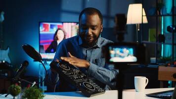 BIPOC content creator filming technology review of newly released DJ controller, unpacking it and presenting specifications to audience. Influencer showing sound mixer to fans photo