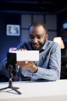 Content creator filming technology review of newly launched digital device, excited to unbox it and present specifications to audience. Online star laughing while showing product to fans photo