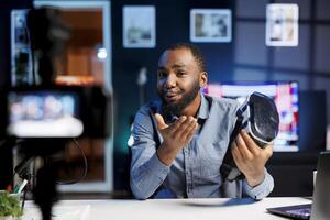 Smiling tech content creator filming technology review of newly released VR glasses, unboxing them and presenting specifications to audience. Influencer showing virtual reality device to subscribers photo
