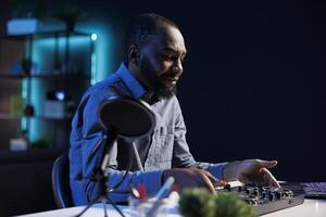 Artist filming DJ mixing tutorial in apartment studio, showing examples of sampling on sound controller to viewers. Entertainer showing modern musical equipment to subscribers in living room photo