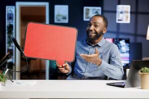 Happy man filming sponsored content, holding empty copy space sign in hand, following script while talking to audience. Viral media star using cardboard bubble speech cutout to do promotion to viewers photo