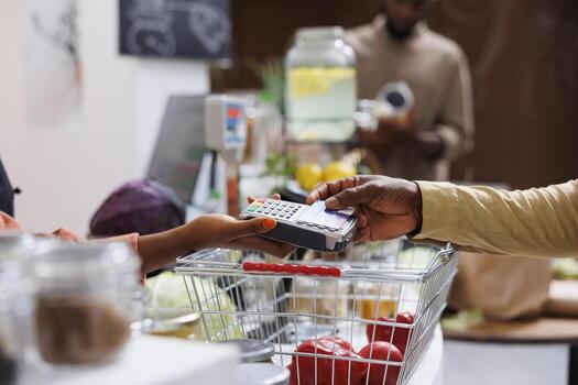 Close-up shot of hand tapping a debit card on the terminal, symbolizing a secure and efficient transaction. Selective focus on African American people utilizing a POS machine for eco-store payments. photo