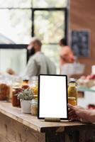 Electronic tablet with white screen is placed in the foreground. It is on a table that is filled with several organic bulk products in reusable jars and containers, promoting a zero-waste initiative. photo