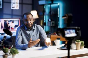 BIPOC influencer recording review of dimmable light bulb able to change into different colors. Tech guru presenting smart home automation technology controlled by voice commands photo