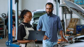Precise mechanic in car service uses laptop to calculate repairments invoice for client after fixing broken parts. Trained expert using device to inform man of final costs after reconditioning vehicle photo
