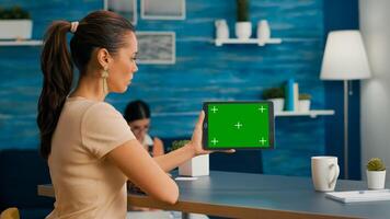 Woman looking at tablet computer with mock up green screen chroma key display browsing on internet searching lifestyle ideas. Freelancer using isolated device standing on desk office in living room photo