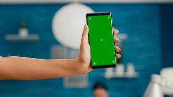 Hands of freelencer holding vertical mock up green screen chroma key smartphone. Business woman using isolated phone for browsing social networks sitting on office desk photo