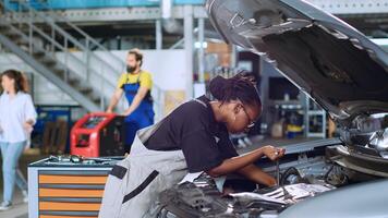 African american mechanic in garage using torque wrench to tighten bolts inside opened up vehicle, preparing to change oil. Auto repair shop expert doing checkup on car to prevent issues photo