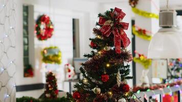 Christmas pine tree adorn with red ornaments in empty office, with blurry background of computer monitors on desks in xmas decorated workplace during winter holiday season photo