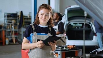 Portrait of smiling mechanic in garage workspace using tablet to order new parts for car after finding damages during annual checkup. Cheerful specialist looking online for automotive components photo