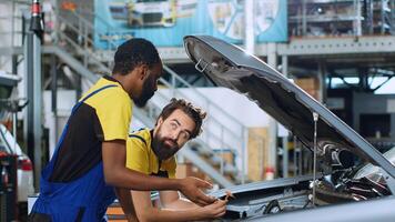 Mechanics in auto repair shop working together on fixing car, discussing best options. Repairman and coworker collaborating on servicing broken vehicle, checking for faulty components photo