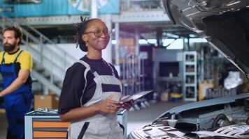 Portrait of smiling engineer doing car maintenance in repair shop using tablet to keep track of operations. Qualified specialist in garage looking over checklist on device while fixing vehicle photo
