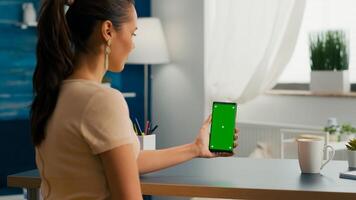 Social media woman holding touchscreen phone with mock up green screen chroma key sitting at modern office desk. Caucasian female working at online app using smartphone with isolated display photo