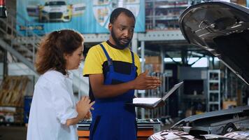 Experienced mechanic using laptop to show woman damaged components found in her car. Qualified repairman using device to help customer visualize repairments that need to be done to vehicle photo