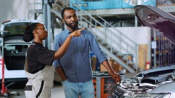 Mechanic in auto repair shop using augmented reality hologram to visualize car parts to african american man. Worker using AR holographic technology to show client vehicle damages photo