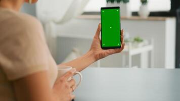 Business woman browsing on internet using mock up green screen chroma key smartphone sitting at office desk. Freelancer swiping online information for social media project using isolated device photo