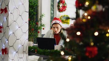 Zoom in shot on focused employee working on overdue project during Christmas season in festive decorated office. Worker in multicultural workplace adorn with red xmas garlands and bows photo
