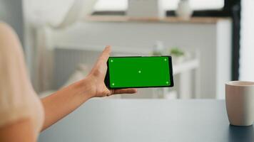 Freelancer holding smartphone with mock up green screen chroma key in horizontal position. Business woman searching online information using isolated device sitting on office desk photo