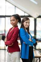 Two diverse businesswomen standing back-to-back, projecting confidence and partnership in a modern office space. photo