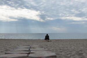 Rear view portrait of a man relaxing sitting on the beach and looking at the sea in the background. High quality photo