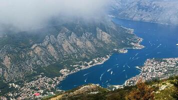 Aerial view of a coastal town and deep blue bay nestled among rugged mountains with distinct rock formations. Fog and clouds photo