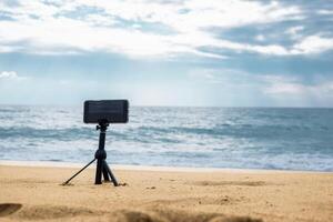 A smartphone camera on a tripod in the foreground stands on the seashore in cloudy weather. High quality photo