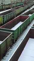 View of the rows with empty containers for the supply of goods, sprinkled with snow on the background of the railway station outside the city. Logistics. Vertical video