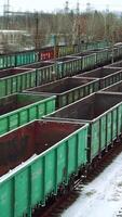 Aerial view on a huge number of iron containers of different colors located at the final station on the background of a freight train, which is moving in their direction. Close-up. Vertical video