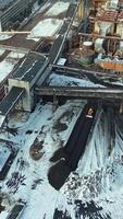 Yellow excavator smoothes black ash from coal under the bridge in the territory of the heating power station. Aerial view. Vertical video