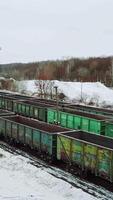 Long rows with old cargo containers for the transport of imports and exports stand on the edge of the forest in the winter on the border zone. Aerial view. Vertical video