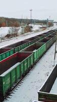 Empty shipping containers are located at an abandoned railway station in the countryside against the background of snow and forest. Aerial view. Vertical video