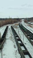 Long rows of containers stand on rails on the territory of the railway. Shipping. Camera motion to back. Aerial view. Vertical video