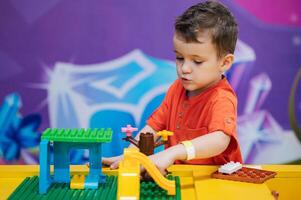 Educational toys. The picture is a plan of a boy's child playing with colorful plastic bricks at a table. The kid has fun and builds from bright constructor cubes. Early learning. photo